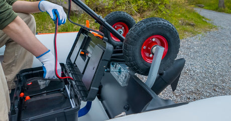 A man wearing gloves kneels down in front of a battery. The battery is sitting inside of a protective casing with wheels on it.