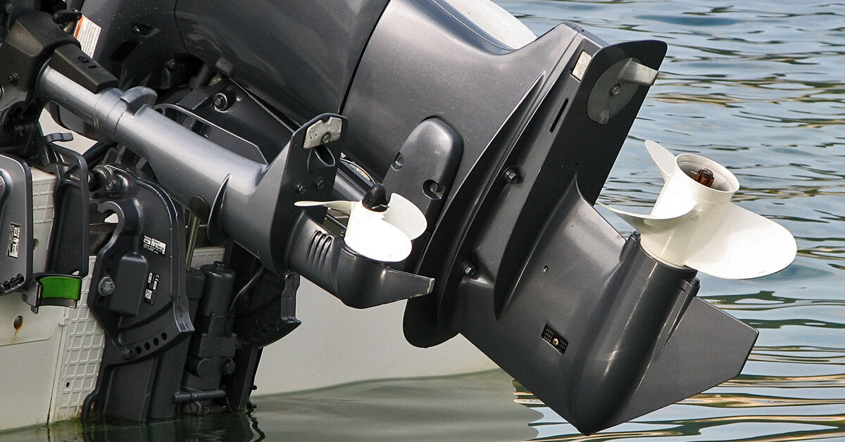 A close-up of the back of a boat that’s stopped on the water with its motor pulled up to show the propellers.
