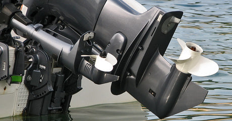 A close-up of the back of a boat that’s stopped on the water with its motor pulled up to show the propellers.