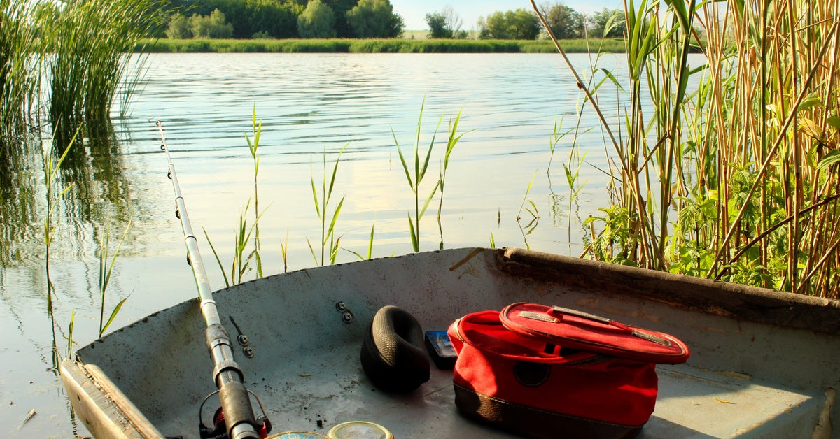 A fishing boat sitting among the reeds on a lake with a pole and other accessories sitting on the edge of the bow.