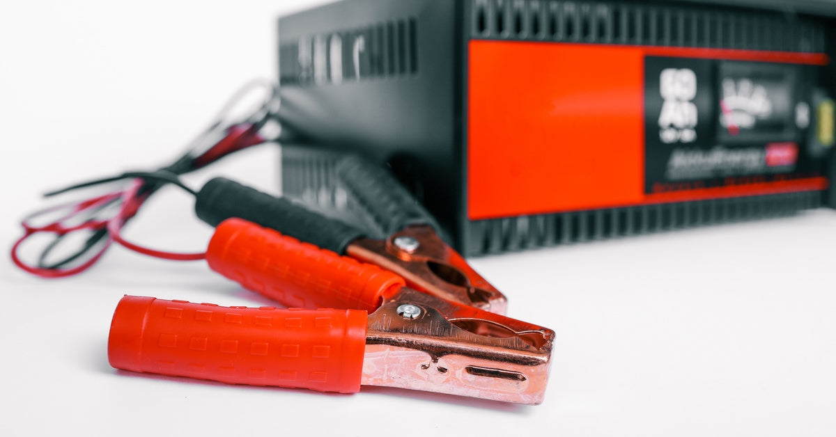 A closeup of red and black jumper cables attached to a charging system over an empty plain white background.