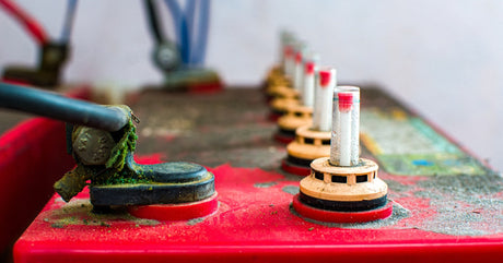 A red battery with wires connected to it and small patches of corrosion all over the casing and terminals.