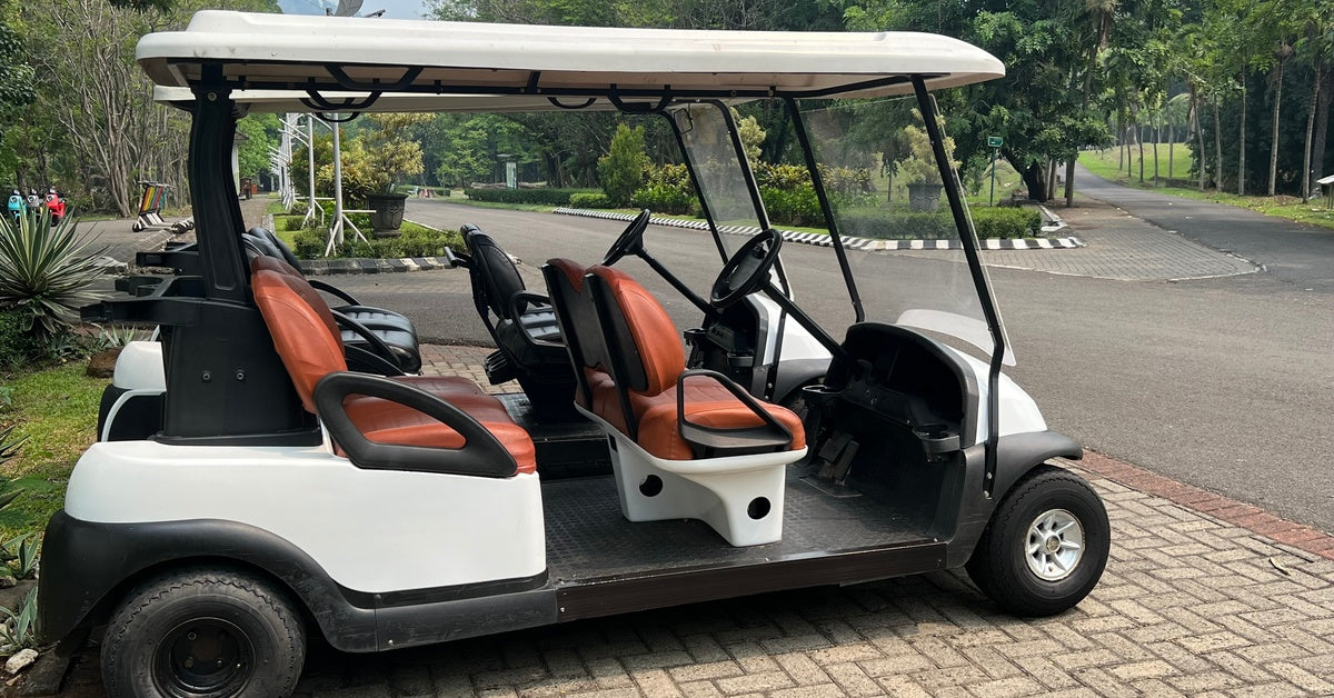 An empty four-passenger golf cart parked in front of a road with a line of trees in the background.
