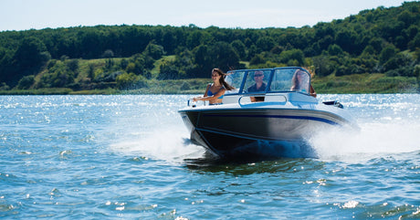 A family enjoying their day while operating a boat on the water with the trees and hills in the background.