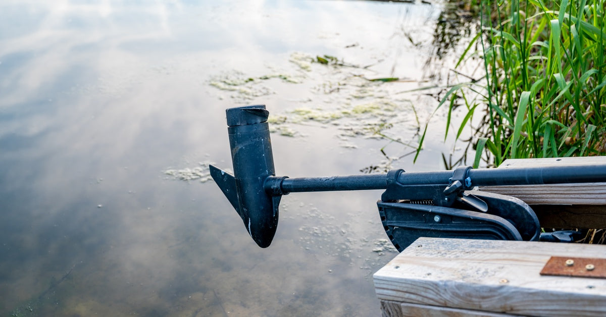 A wooden boat resting on the grass, its trolling outboard motor extended above murky, moss-covered water.