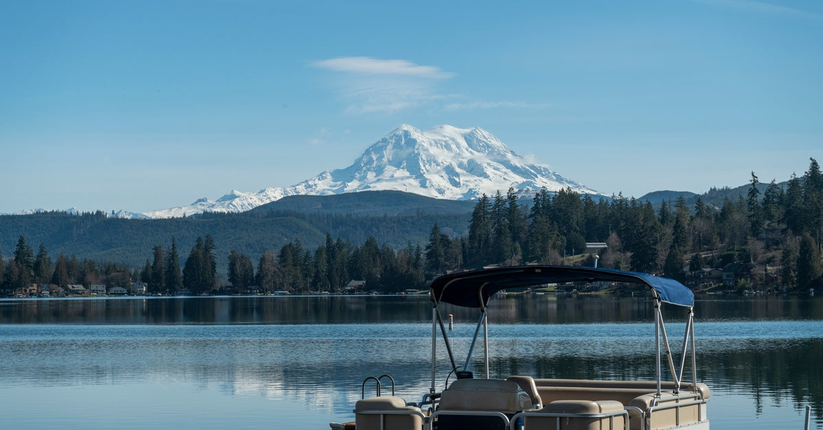 A pontoon sitting on the clear surface of a lake in Washington. Mount Rainier is visible in the distance with snowy caps.