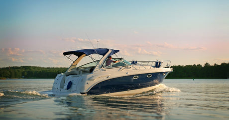 A man is driving a large white and blue boat on the water. The boat has a blue canopy and below-deck windows.