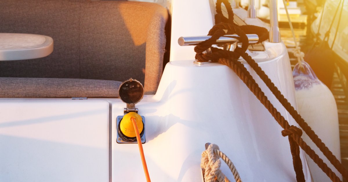 An orange charging cord is plugged into the back of a white boat. A black rope is tied around a hook.