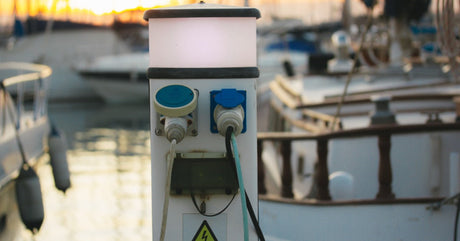 A charging station sits on a wooden dock with two charging cables plugged into it. A circular light is on top of the station.