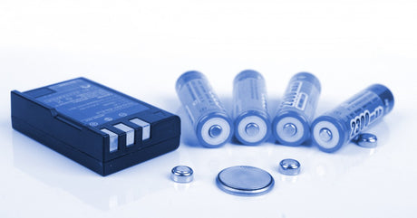 Various types of lithium-ion batteries are sitting together over a white background with a slightly blue highlight on them.