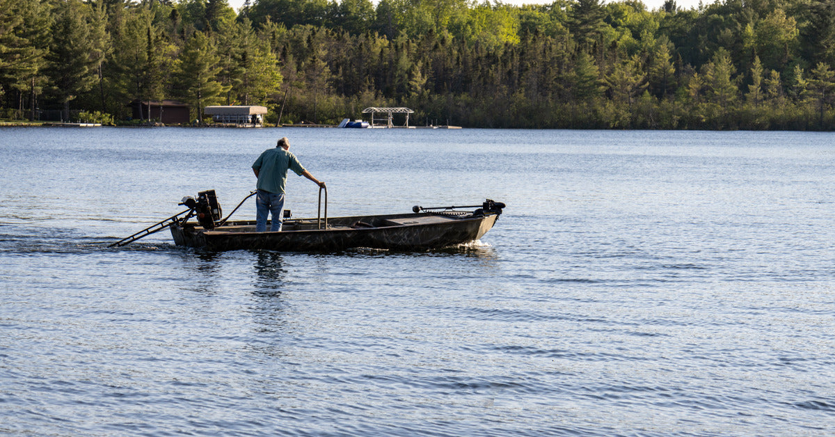 A person on a lake in a fishing boat using a trolling motor to move while holding onto a large metal bar.