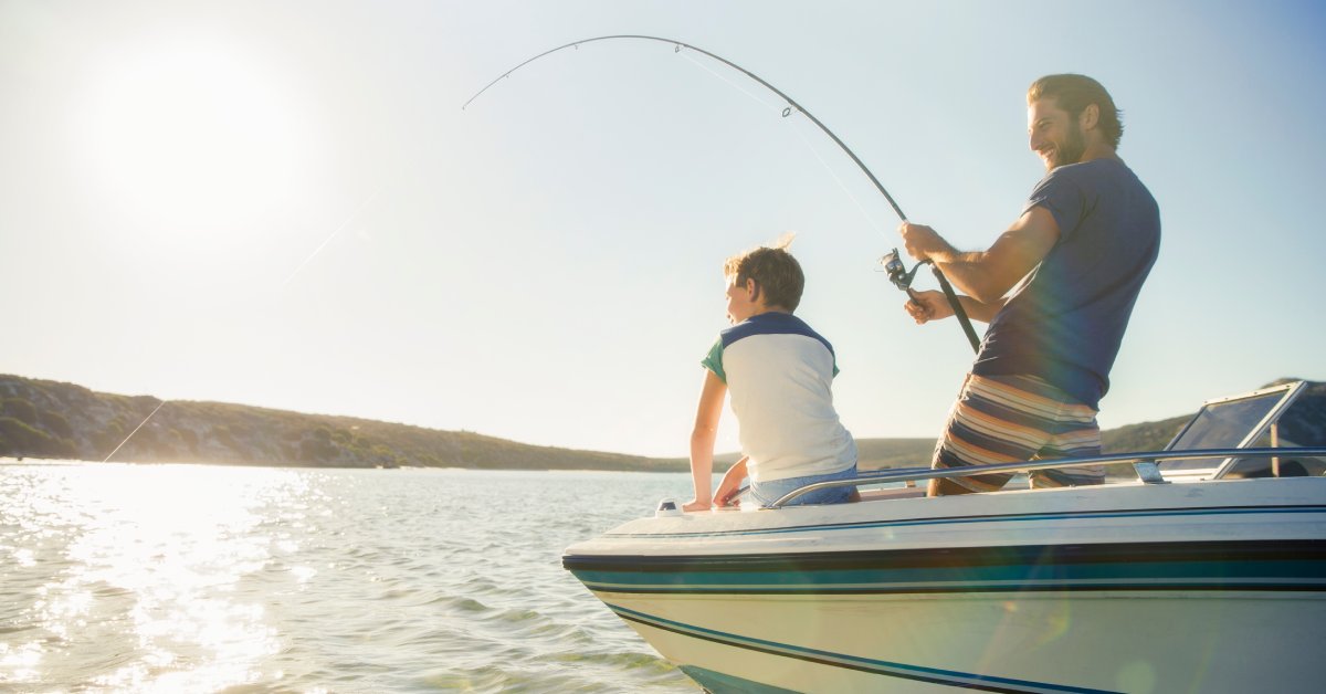 A man and his son in a boat on the water during a fishing trip. The man is holding a fishing rod and the line is in the water.