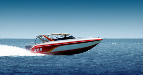 A red and white speedboat moving quickly over the water with a wake behind the engine and a blue sky above.