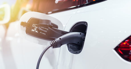 The side of a white electric car parked while using a power charger to refill the battery during the day.