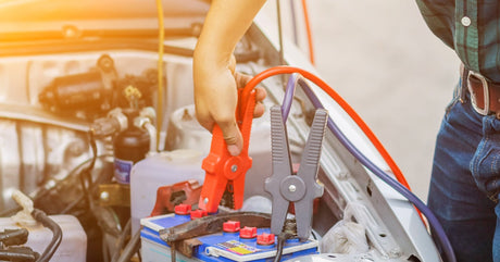 A man standing over a battery on a boat connecting a red wire to one of the terminals with a gray wire already attached.