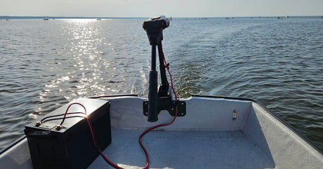 A large black battery sits on a boat and is connected to a tall, skinny motor. The boat is on the water.
