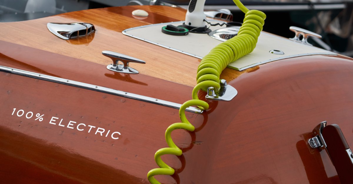 A coiled yellow cord connecting a charger to the port of an electric boat with a wooden finish and chrome details.