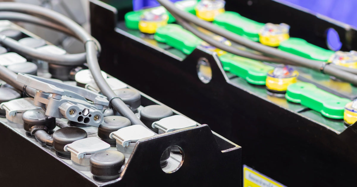 A pair of narrow automotive batteries with metal black shells and gray connector wires resting on top of them.