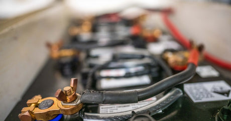 A close-up view of a series of marine batteries. The batteries are black and have metallic connections.