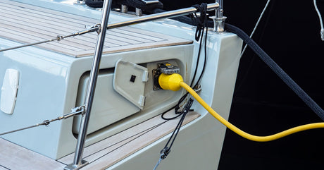 A yellow charging cord reaching over the water to connect with a ship's on-board charging port to give it power.