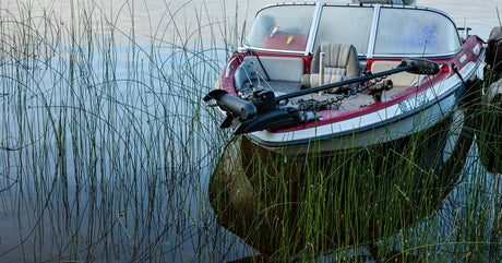 A red-and-white boat with a trolling motor lifted out of the water. The boat is currently tied up and still.
