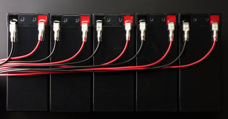 A row of black batteries, each connected to a red wire and a black wire. The wires all gather to the left of the row.