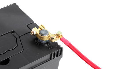 A black automotive battery with a red cable attached to its positive pole. The battery sits against a plain white background.