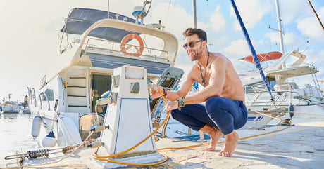 A person crouching down by a marine charging station and investigating the cord that leads to their boat.