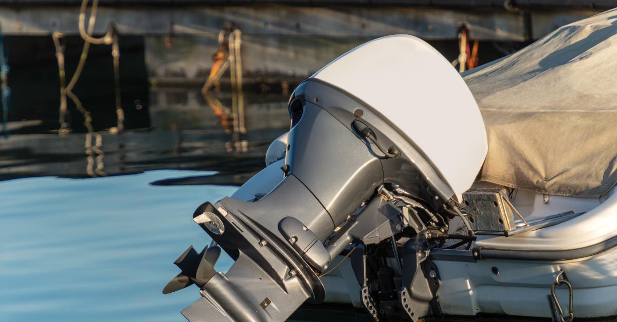 An outboard boat motor in its lifted position, keeping it out of the water. The boat is off and covered with a tarp.