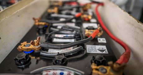 A group of four-to-five black boat batteries connected by their terminals. The batteries are in an enclosed area.