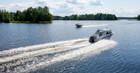 A pair of small boats moving across the surface of a calm lake on a bright, sunny day and leaving white wakes behind them.